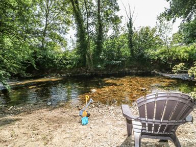 A plastic chair and children's sand toys on the edge of a river surrounded by trees at Crannacombe Farmhouse in Loddiswell