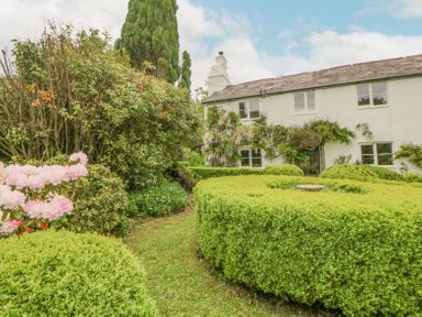 A garden with trimmed hedges and flowering bushes in front of a two story white house at Crannacombe Farmhouse in Loddiswell