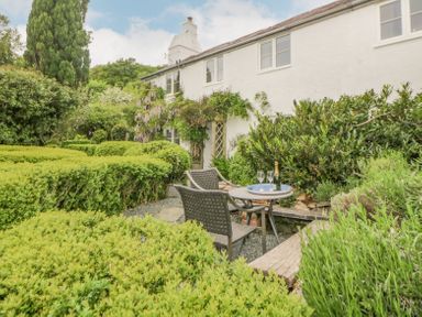 A garden with trimmed hedges a table and two chairs with a bottle and glasses outside a white farmhouse at Crannacombe Farmhouse in Loddiswell