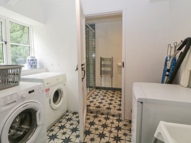 A laundry room with washing machines an ironing board and a door leading to a bathroom at Crannacombe Farmhouse in Loddiswell