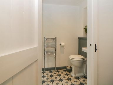 A bathroom with a toilet a towel rack and patterned floor tiles at Crannacombe Farmhouse in Loddiswell