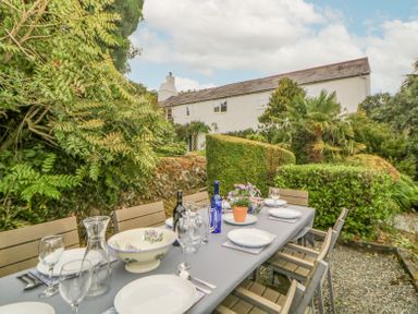 An outdoor dining table set with plates glasses and bottles surrounded by trees and bushes at Crannacombe Farmhouse in Loddiswell