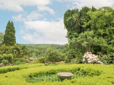 A garden with a birdbath surrounded by hedges and various trees at Crannacombe Farmhouse in Loddiswell