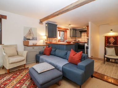 A living room with a blue sofa and red pillows next to a kitchen with blue cabinets and tiled backsplash at The Cider Barn in Loddiswell