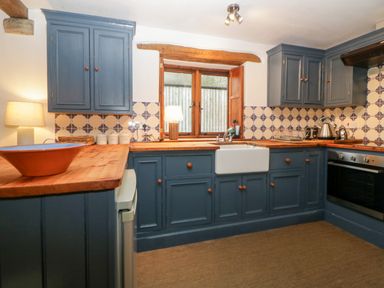 A kitchen with blue cabinets wooden countertops a white sink and tiled backsplash at The Cider Barn in Loddiswell