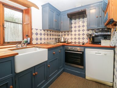 A kitchen with blue cabinets wooden countertops a white sink oven dishwasher and a window at The Cider Barn in Loddiswell