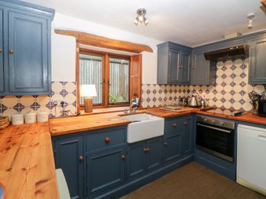 A kitchen with blue cabinets wooden countertops sink oven and window at The Cider Barn in Loddiswell