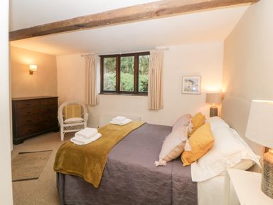 A bedroom with a bed, pillows, blanket, lamps, window, chest of drawers, and a chair at The Cider Barn in Loddiswell