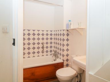 A bathroom with a bathtub tiled with blue and white patterns a toilet and a sink with a shelf above at The Cider Barn in Loddiswell