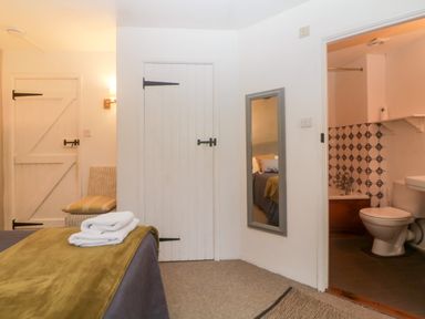 A bedroom with a bed folded towels a chair a wall mirror a wooden door and an open door leading to a bathroom with a toilet and bathtub at The Cider Barn in Loddiswell