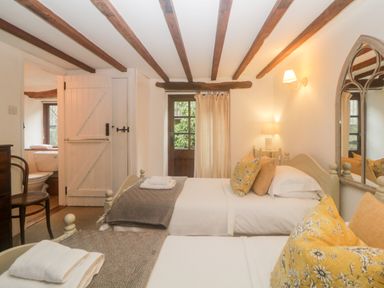 A bedroom with two single beds a wooden chair a door to a bathroom and wooden ceiling beams at The Cider Barn in Loddiswell