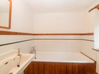 A bathroom with a bathtub and a sink with a mirror above at The Cider Barn in Loddiswell