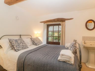 A bedroom with a metal bed frame pillows blanket a wooden door a small window a wall-mounted sink and a round mirror at The Cider Barn in Loddiswell
