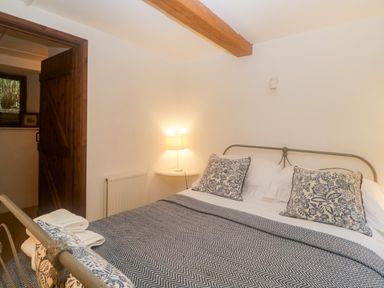 A bedroom with a metal bed frame bed with patterned pillows and a blanket a corner shelf with a lamp and an open wooden door at The Cider Barn in Loddiswell