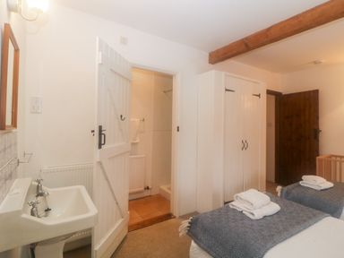 A bedroom with two beds and towels on them a wooden crib a white wardrobe a white sink an open door leading to a bathroom at The Cider Barn in Loddiswell