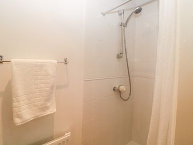 A bathroom with a shower area white tiled walls a showerhead a white shower curtain and a towel hanging on a rack at The Cider Barn in Loddiswell