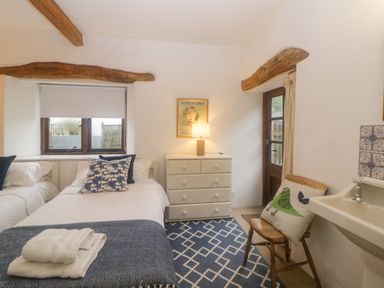 A bedroom with two single beds a wooden chair with a cushion a chest of drawers and a sink at The Cider Barn in Loddiswell