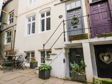 An outdoor patio with a metal table and chairs and several potted plants in front of a building with multiple doors in Robins Nest Whitby