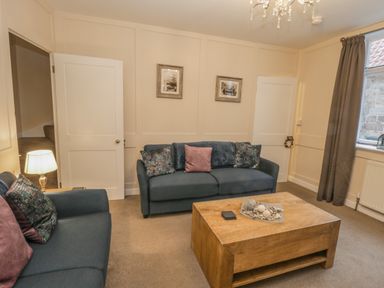 A living room with blue sofas a wooden coffee table a lamp and pictures on the wall at Robins Nest in Whitby