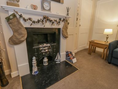 A fireplace with stockings and garland decorations a clock on the mantle a lamp on a wooden side table and a blue sofa in a living room at Robins Nest in Whitby