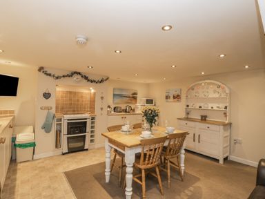A kitchen with a wooden dining table and four chairs a stove a microwave a white cabinet with decorative plates and wall paintings at Robins Nest in Whitby
