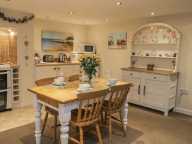 A dining area with a wooden table and chairs set with bowls and glasses and a floral centerpiece at Robins Nest in Whitby