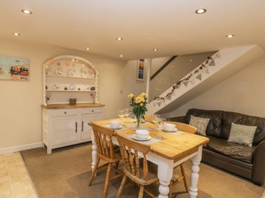 A dining area with wooden table and chairs a brown leather sofa and a white cabinet with plates at Robins Nest in Whitby