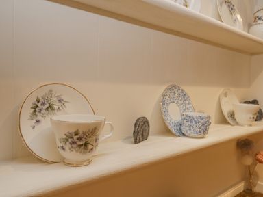 A shelf with floral patterned teacups and saucers and small rocks at Robins Nest in Whitby
