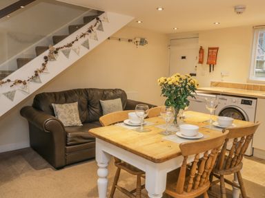 A dining table with chairs and tableware next to a sofa under stairs in a kitchen area at Robins Nest in Whitby