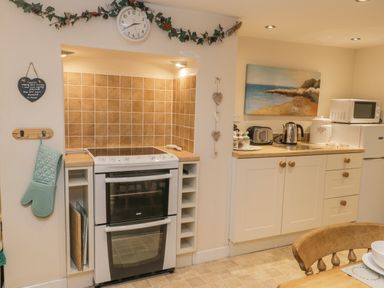 A kitchen with a white stove and oven a microwave and toaster on countertops and a wooden dining chair Robins Nest Whitby