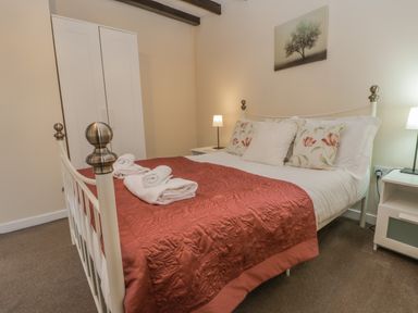 A bedroom with a double bed with floral pillows and folded towels on a red quilt at Robins Nest in Whitby