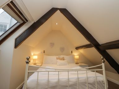 A bedroom with a white metal bed and bedside tables with lamps under a sloped ceiling with dark wooden beams at Robins Nest in Whitby