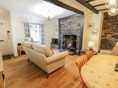 A living room with beige sofas a wood burning stove stone fireplace wooden dining table and chairs at Ty Coed in Llanberis