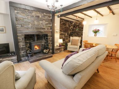 A living room with a stone fireplace a stove beige sofas a wooden dining table and chairs and flowers in a vase at Ty Coed in Llanberis