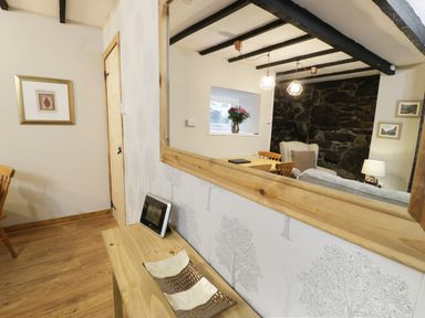A wooden table with a digital clock and decorative tray below a large mirror reflecting a dining area with chairs flowers and a stone wall at Ty Coed in Llanberis