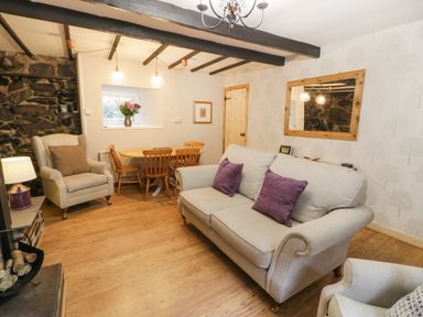 A living room with a sofa and armchair a dining table with chairs a window and a large mirror at Ty Coed in Llanberis