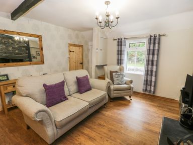 A living room with beige sofa and armchair with cushions wooden floor window with plaid curtains and a wooden door at Ty Coed in Llanberis