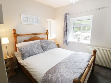 A bedroom with a wooden bed with gray floral bedding beside two wooden bedside tables with lamps at Ty Coed in Llanberis