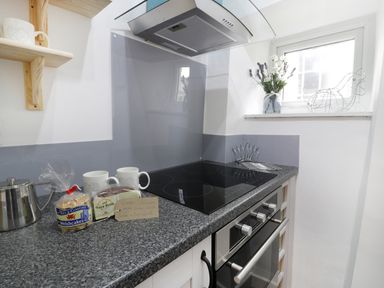 A kitchen countertop with an electric stove two mugs packaged Welsh cakes and Bara Brith a teapot and a small window with flowers and a wire chicken decoration at Ty Coed in Llanberis