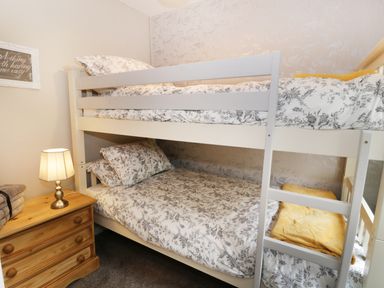 A bedroom with white bunk beds with floral bedding a wooden nightstand with a lamp and folded towels at Ty Coed in Llanberis