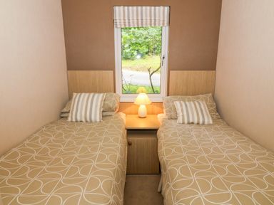 A bedroom with two single beds separated by a nightstand with a lamp under a window at Willow Lodge in Troutbeck Bridge