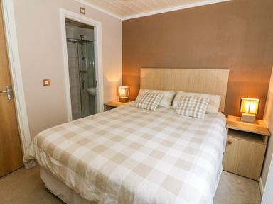 A bedroom with a double bed two bedside tables with lamps and an open door showing a bathroom at Willow Lodge in Troutbeck Bridge