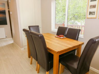 A dining area with a wooden table and six dark brown chairs near a window at Willow Lodge in Troutbeck Bridge