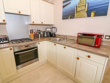 A kitchen with white cabinets a gas stove an oven a sink a red microwave and various kitchen utensils at Willow Lodge in Troutbeck Bridge