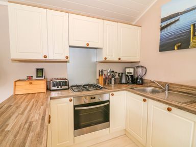 A kitchen with white cabinets a gas stove an oven a toaster kettle coffee maker blender and a sink at Willow Lodge in Troutbeck Bridge