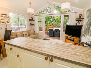 A living area with a sofa a television and sliding doors leading to a patio at Willow Lodge in Troutbeck Bridge