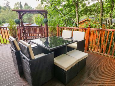 An outdoor deck with a glass-top dining table and cushioned chairs surrounded by wooden railing at Willow Lodge in Troutbeck Bridge