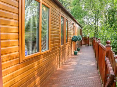 A wooden exterior corridor with windows and potted plants overlooking trees at Willow Lodge in Troutbeck Bridge