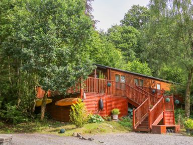 A wooden cabin with stairs and railing surrounded by trees at Willow Lodge in Troutbeck Bridge