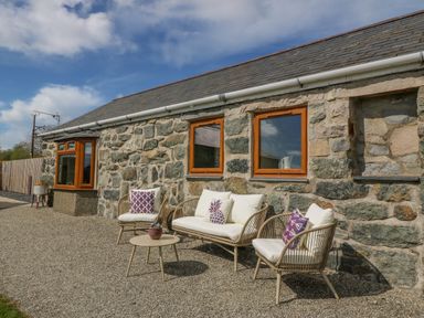 An outdoor seating area with chairs and a table against a stone wall at Beudy in Chwilog